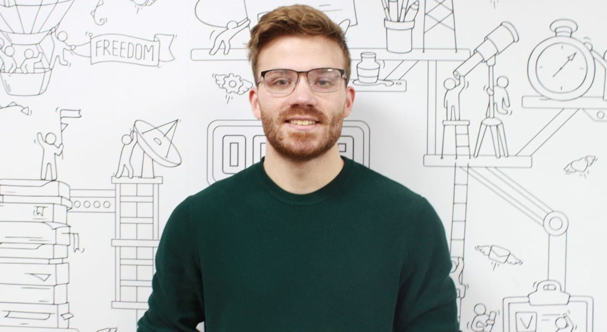 Bearded male wearing glasses and a black top against a background of line drawings